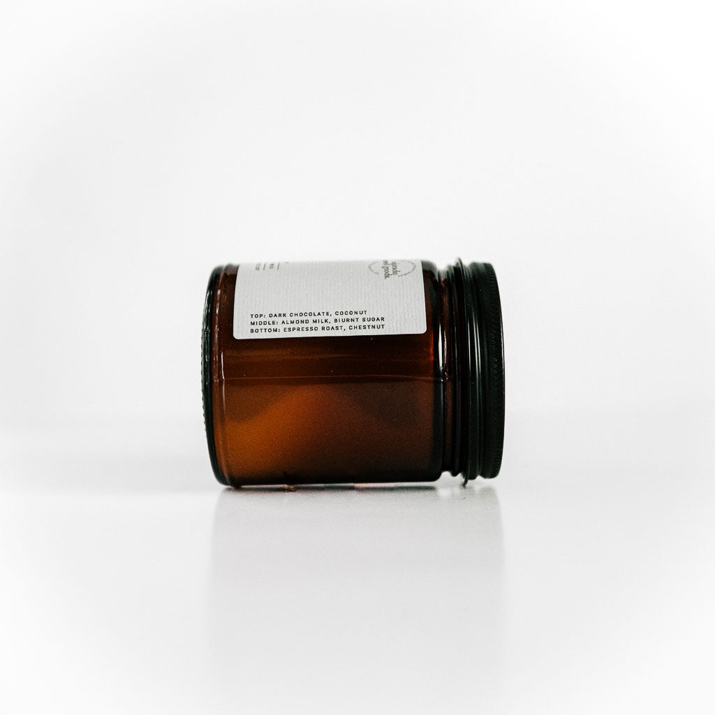 Amber jar scented candle with earthy textures label, matte black lid. Label includes candle name, description